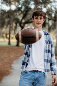 senior boy holding a football in a flannel shirt
